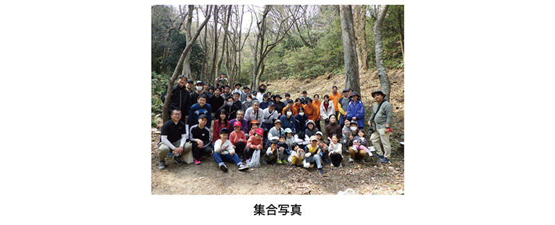 森林の中で多人数が集まり、子どもから大人までが並んで撮影した植樹活動の集合写真